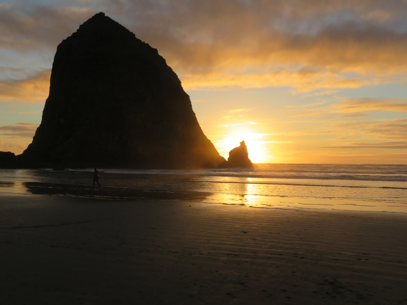 the sun sets behind Haystack Rock lighting up the sky and ocean