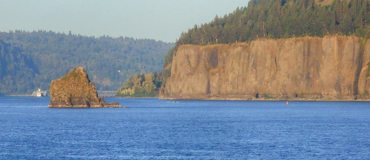 Small pointed rock in the river not far from a large basalt cliff