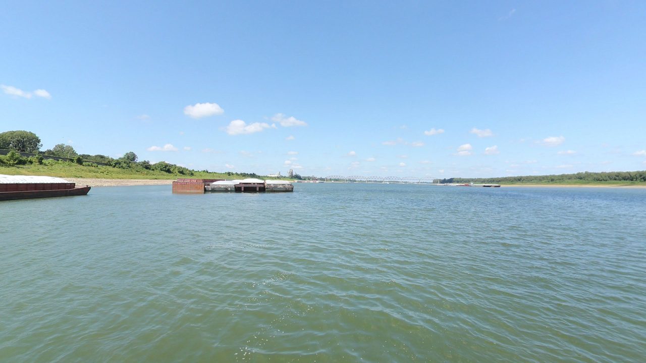 The broad Ohio River with moored barges on the left and a truss bridge on the horizon, 2023