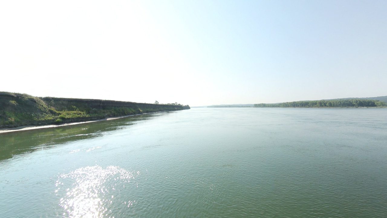 The wide Missouri River below a long, grassy bluff on the left, with sunlight glinting on the water, 2021