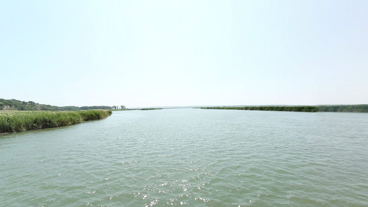 The wide Missouri River beside tall marsh grass on the left, under a hazy sky, 2021