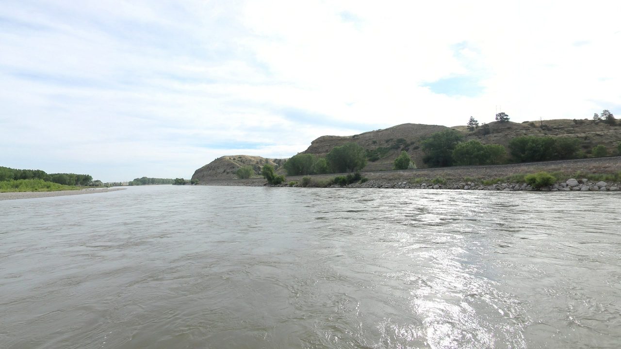 The Yellowstone River below grassy bluffs, with a rock-lined embankment along the right bank, 2024