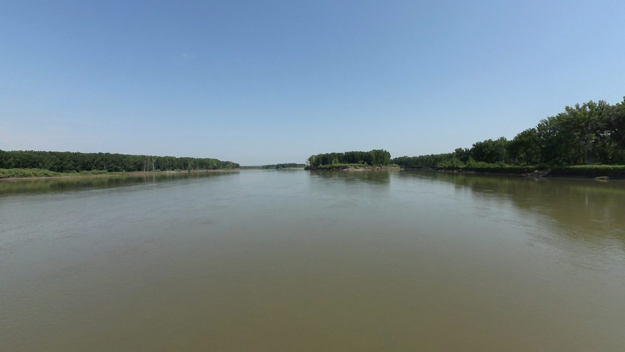 The calm Yellowstone River between wooded banks under a clear sky, 2024