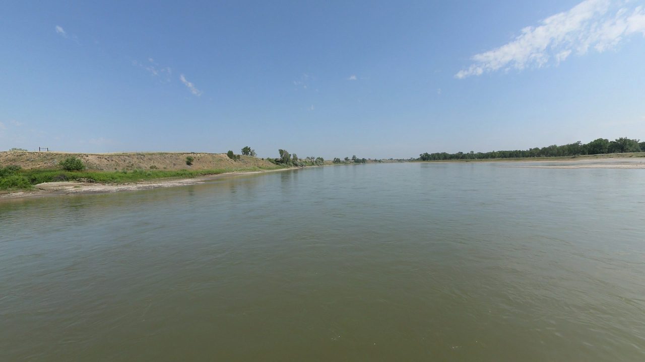 The broad Yellowstone River beside a gravel bank on the left, under a blue sky, 2024