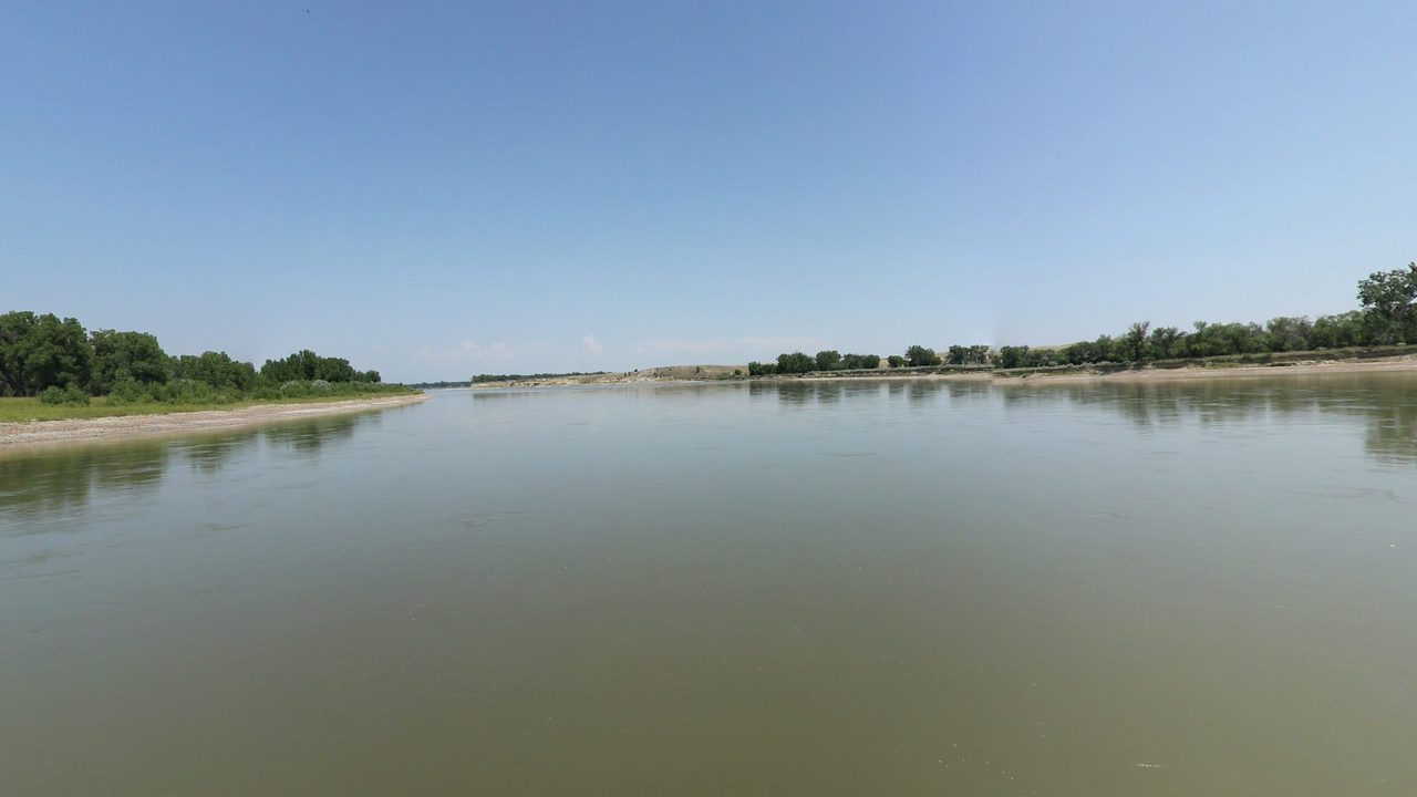 The calm Yellowstone River between low banks and cottonwoods under a clear sky, 2024