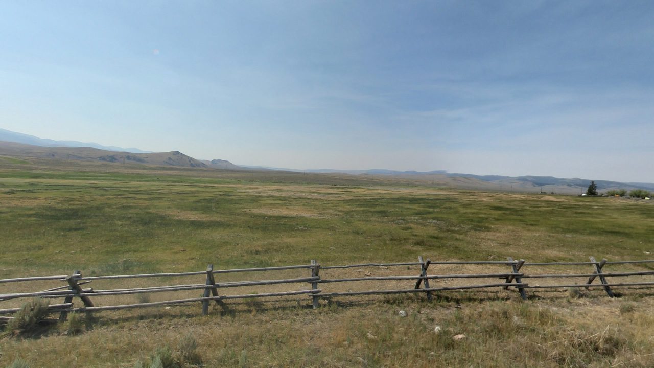 A broad green valley behind a weathered rail fence, with dry hills and distant mountains, 2024