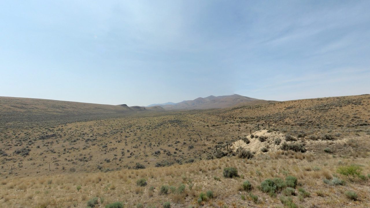 Sagebrush hills rolling toward distant mountains under a hazy sky, 2024