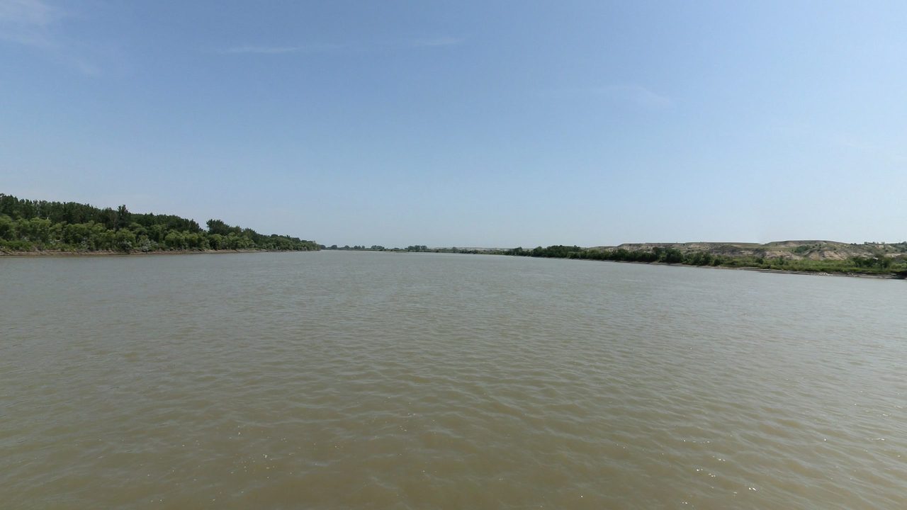 The wide Missouri River between low wooded shores under a pale blue sky, 2024