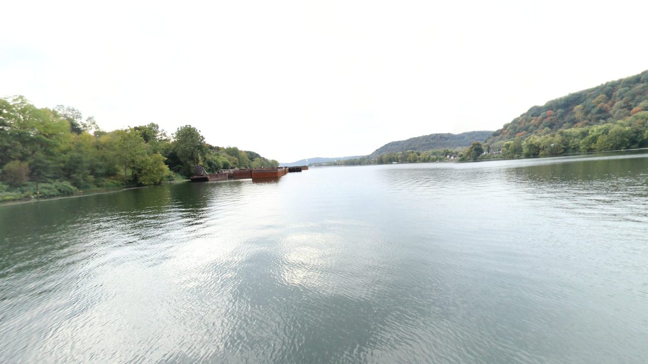 The wide Ohio River under a white sky, with moored barges below wooded hills on the left, 2024