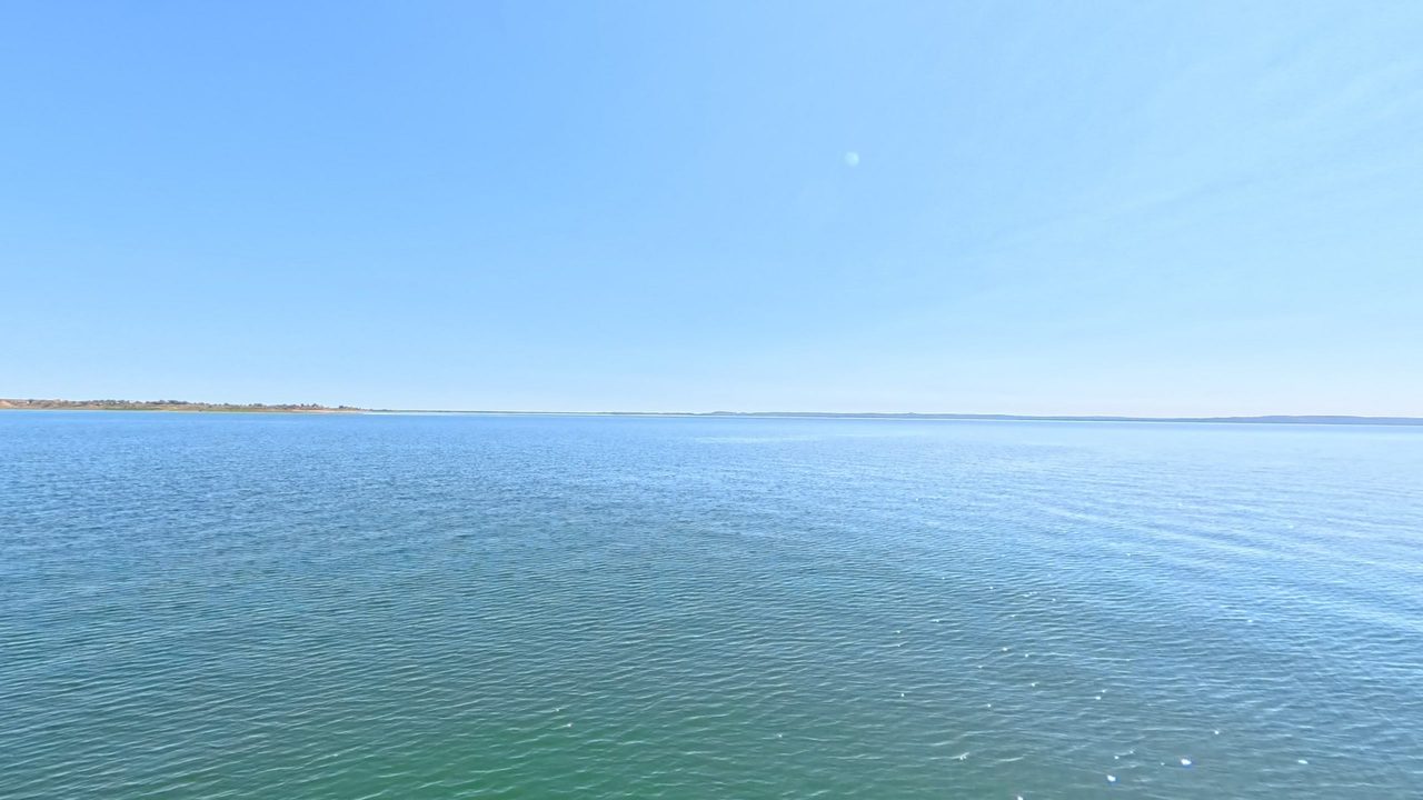 Open blue water stretching to a distant, low shore under a clear sky, 2025