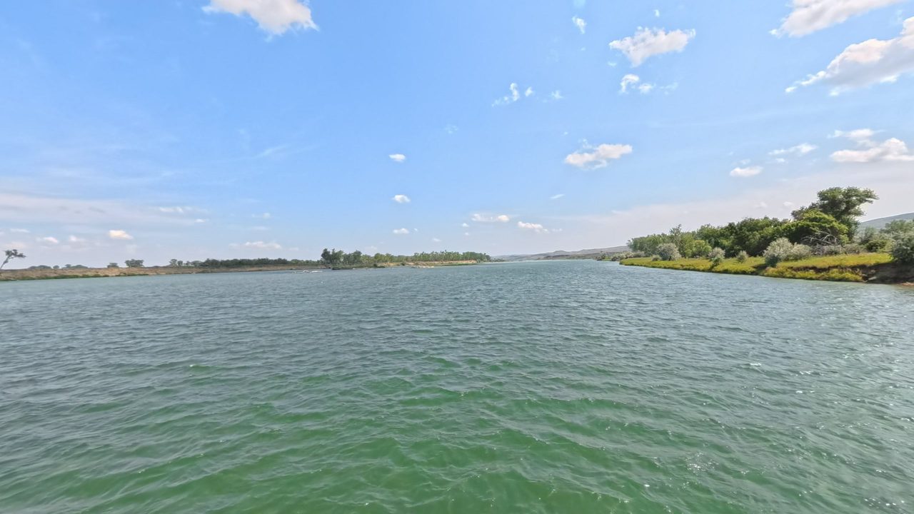 The Missouri River in clear green water, with a small wooded point on the right, 2025