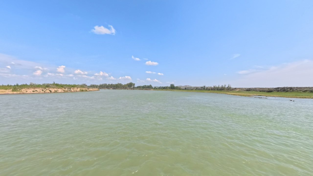 The wide Missouri River in pale green water, with low sandy banks under a blue sky, 2025