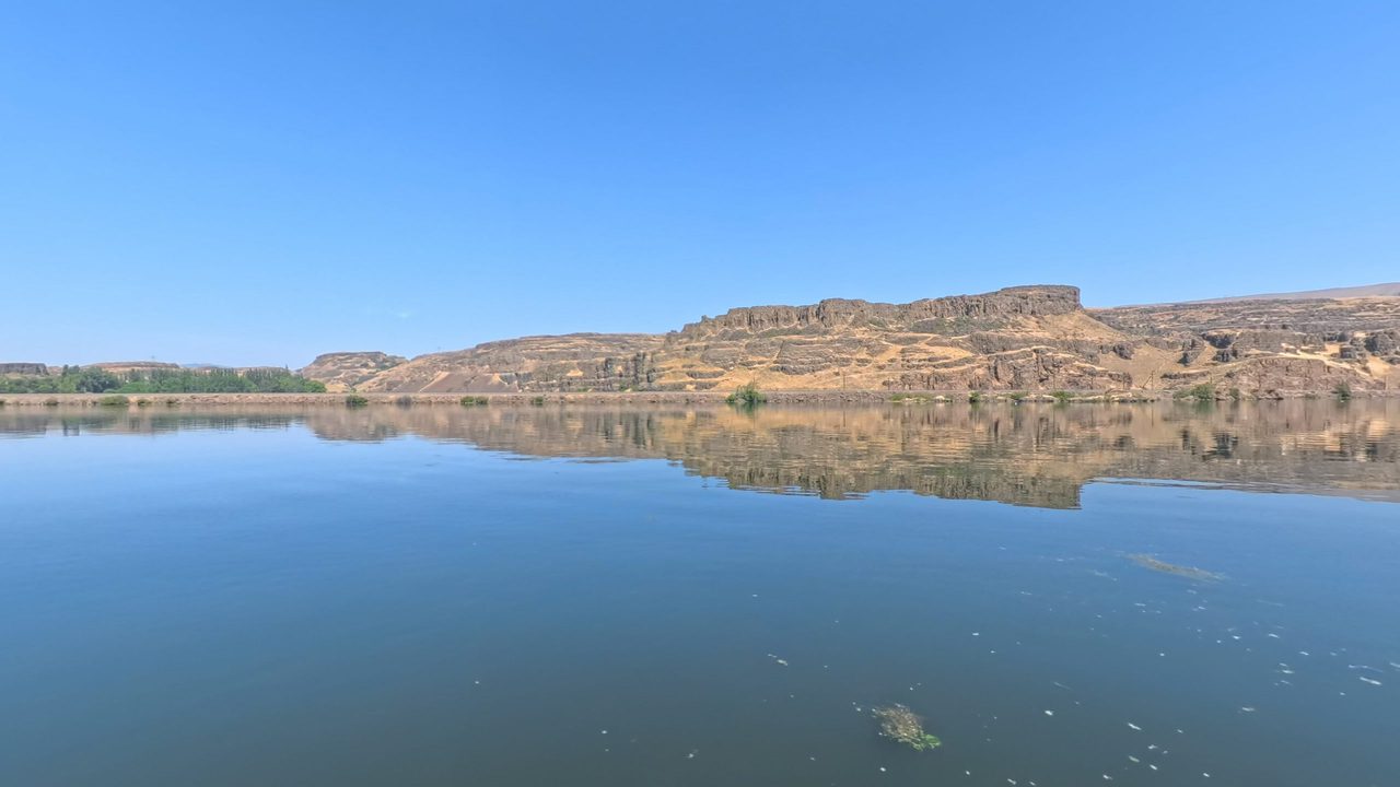 The calm Columbia River reflecting columnar basalt cliffs and dry slopes, 2025