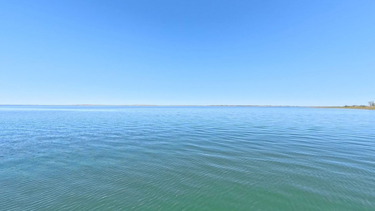 Open blue-green water stretching to a distant shore under a clear sky, 2025