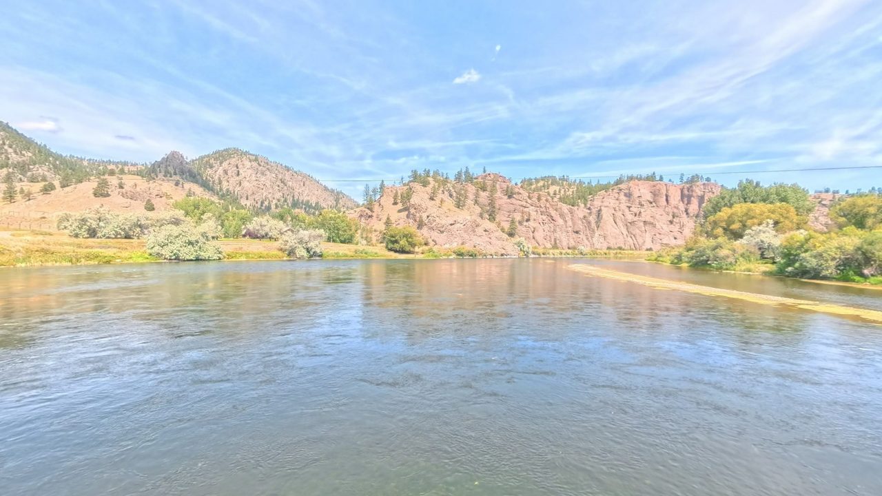 The Missouri River curving past a gravel bar below pink granite cliffs, with silvery shrubs and cottonwoods on the banks, 2025