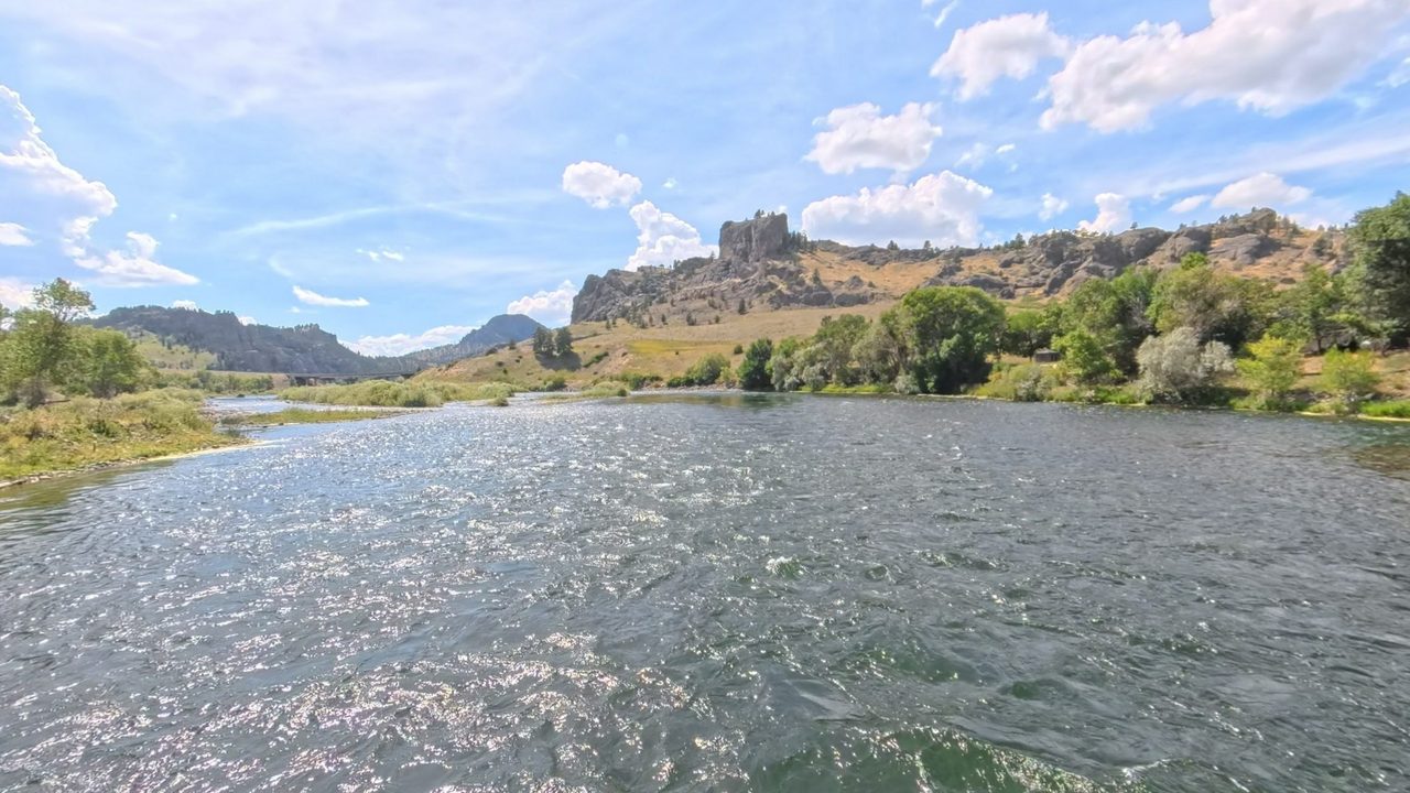 The sunlit Missouri River braiding around grassy islands toward rocky hills and a distant bridge, 2025