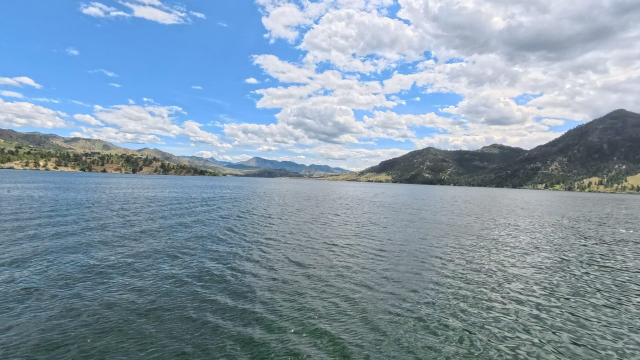 The Missouri River below forested hills and distant mountains, under billowing white clouds, 2025
