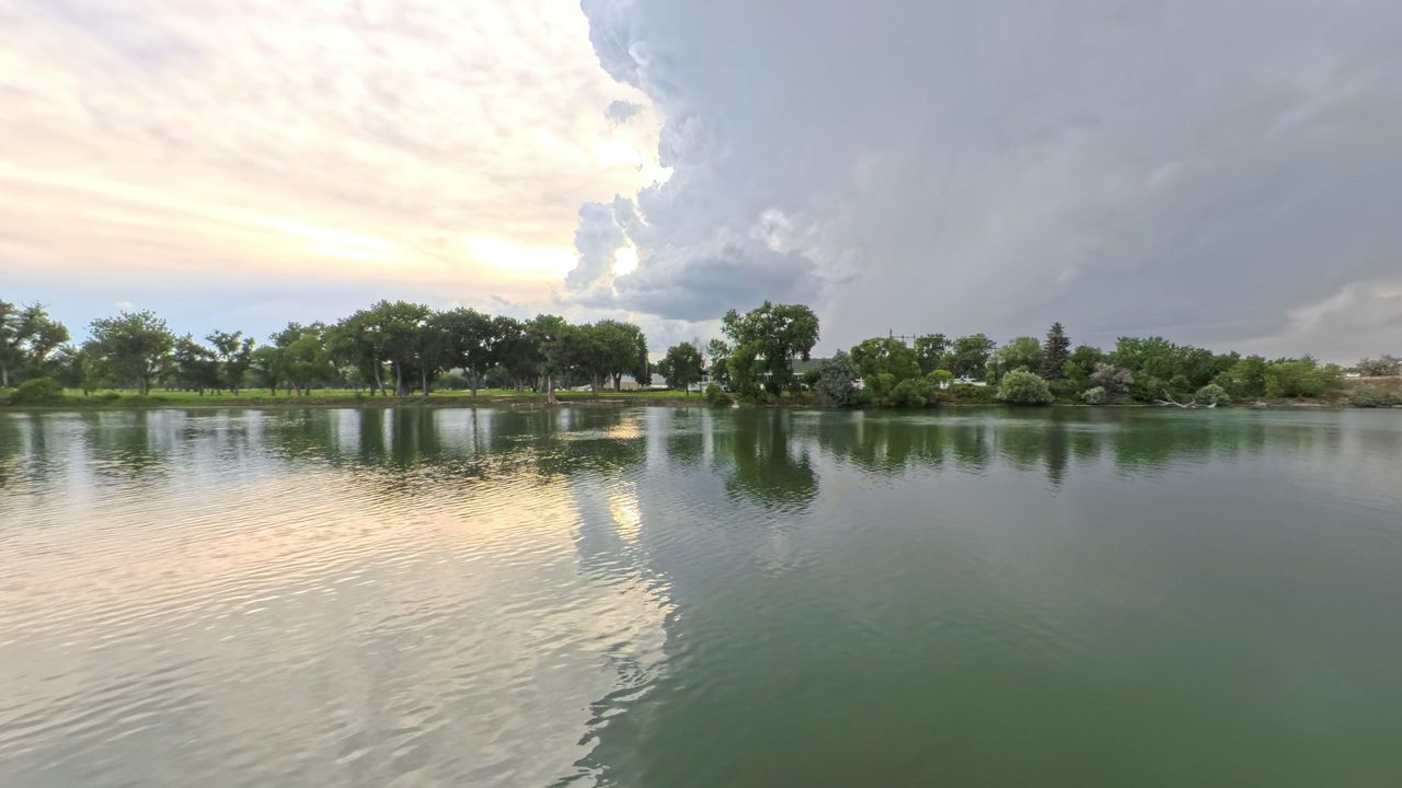 The Missouri River reflecting a towering storm cloud, with trees along the far bank, 2025