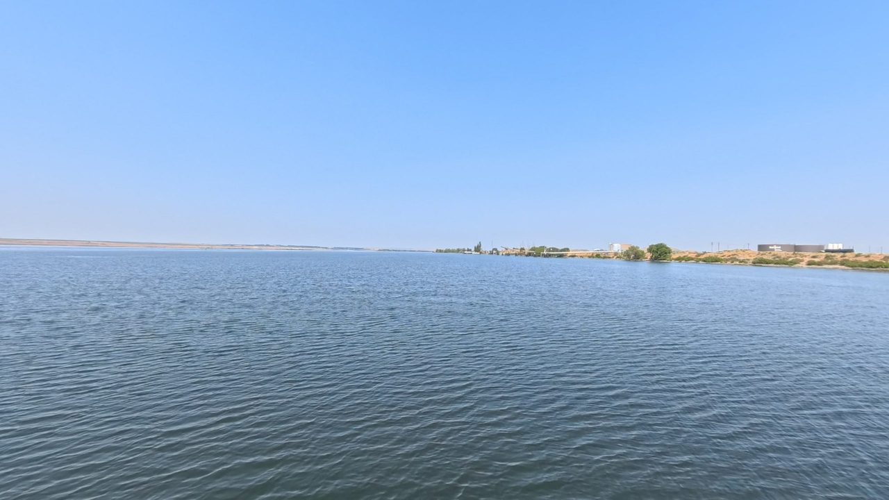 The wide Columbia River under a clear sky, with buildings along the distant right shore, 2025
