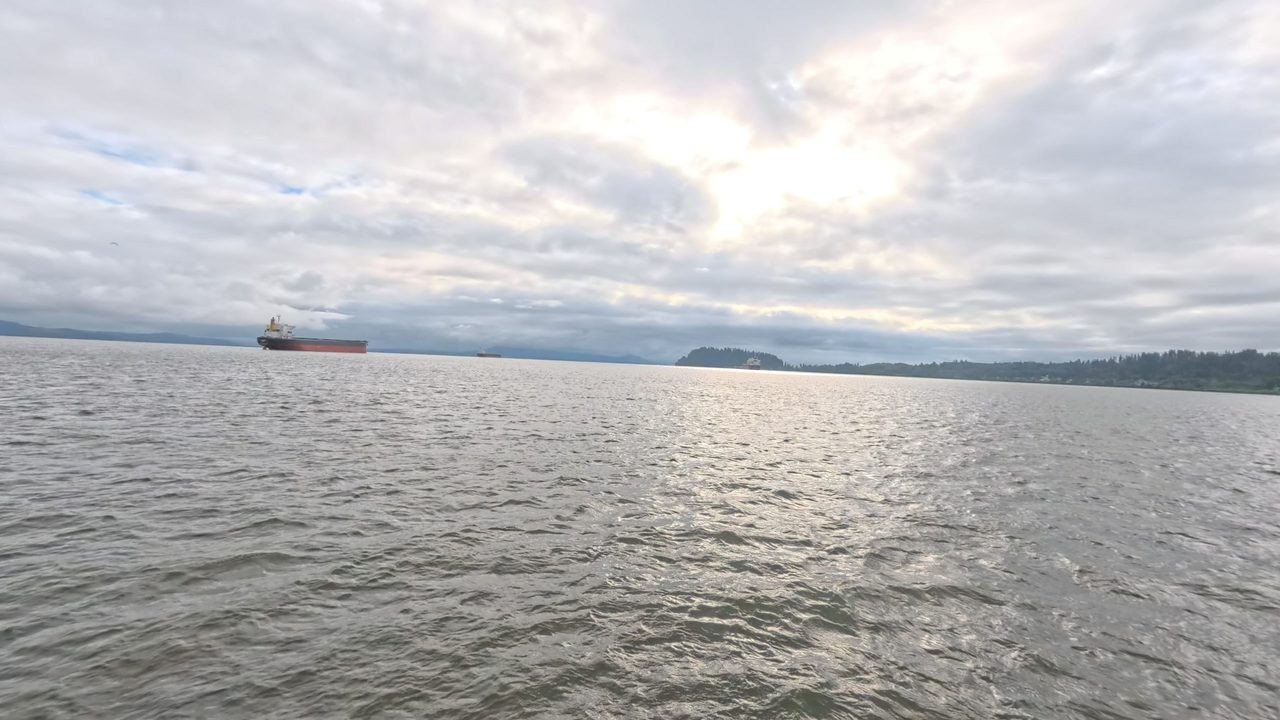 The wide Columbia River under a cloudy sky, with a cargo ship and a forested shoreline, 2025