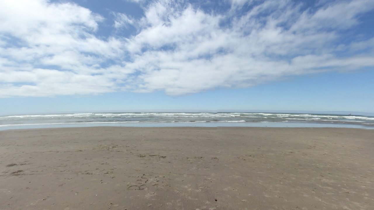 Ocean surf breaking on a wide, flat sand beach under streaks of white cloud, 2025