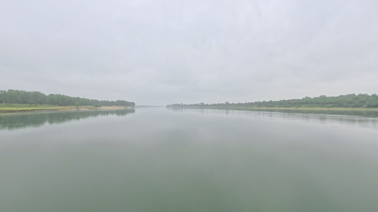 The calm Missouri River between low wooded banks under a grey, overcast sky, 2025