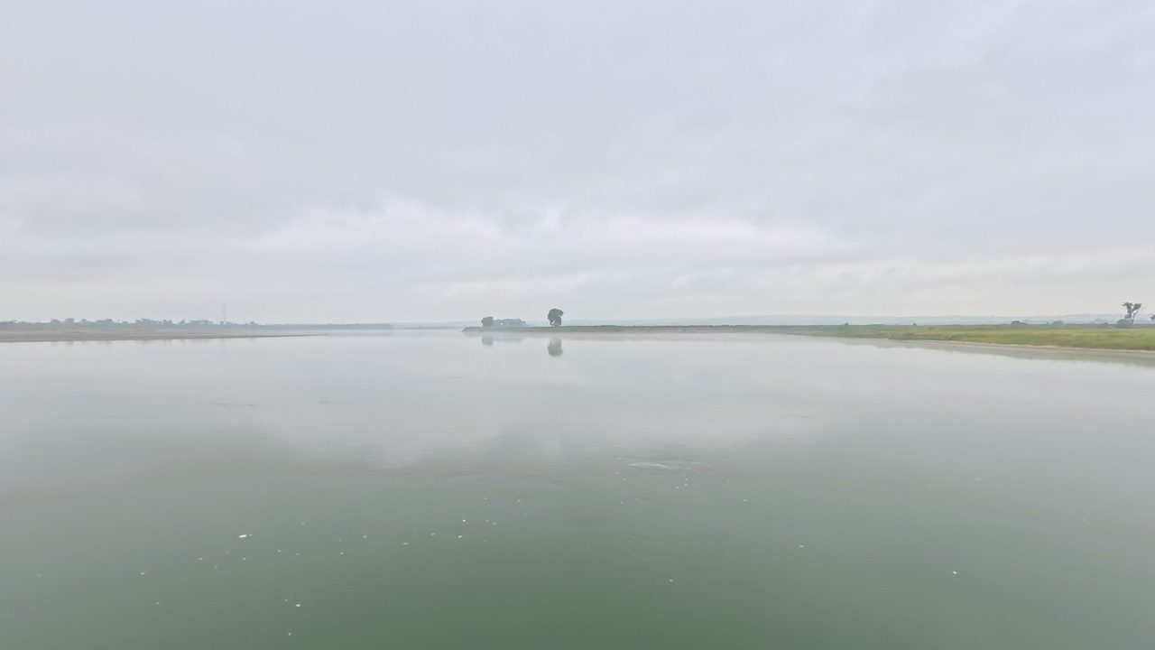 The calm, wide Missouri River under a grey, overcast sky, with low shores in the distance, 2025