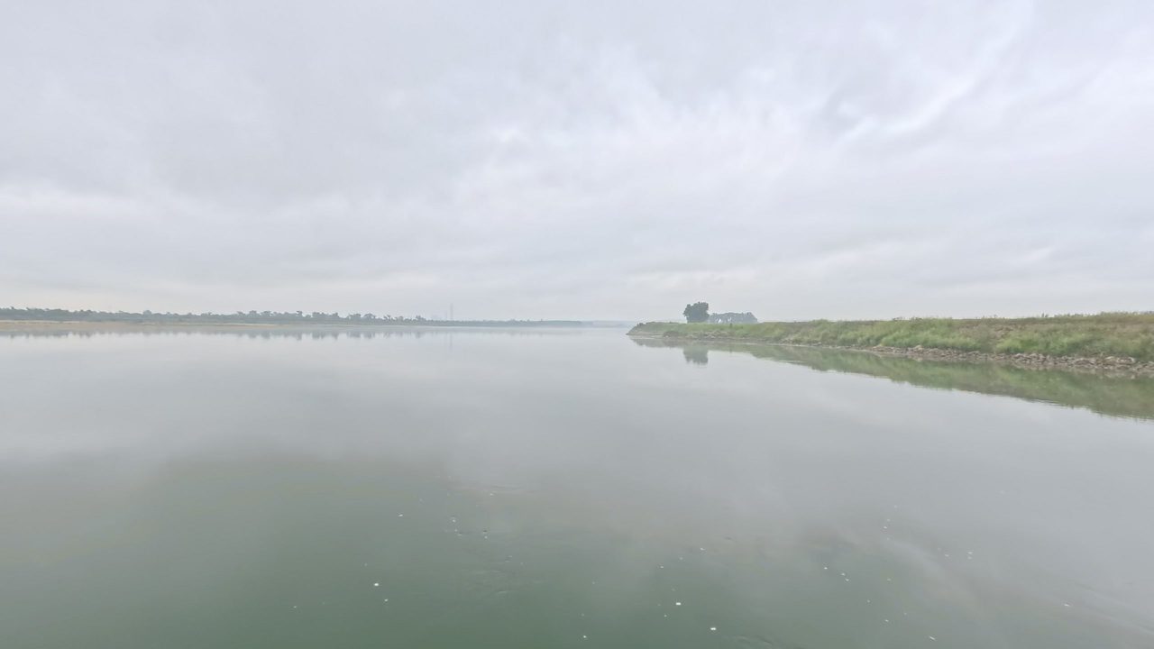 The Missouri River lying still under an overcast sky, with a grassy bank on the right, 2025