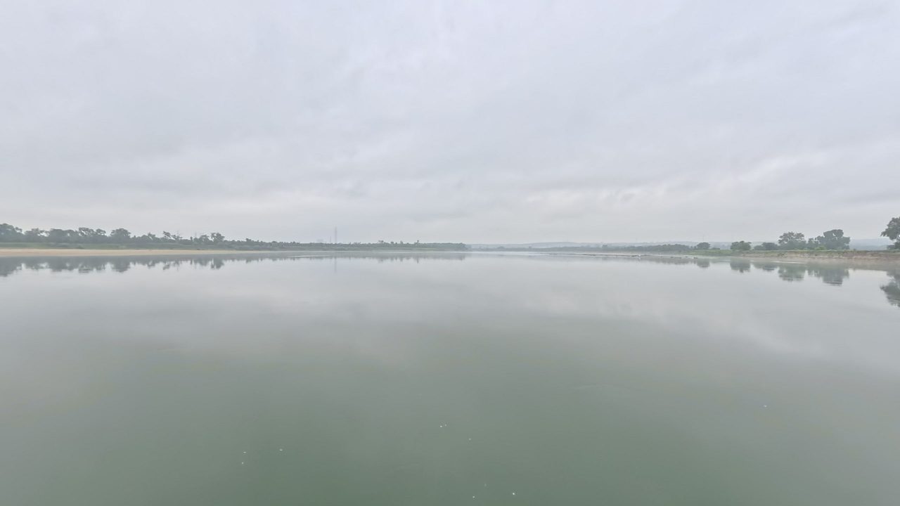 The glassy Missouri River under a grey overcast sky, with low wooded banks, 2025