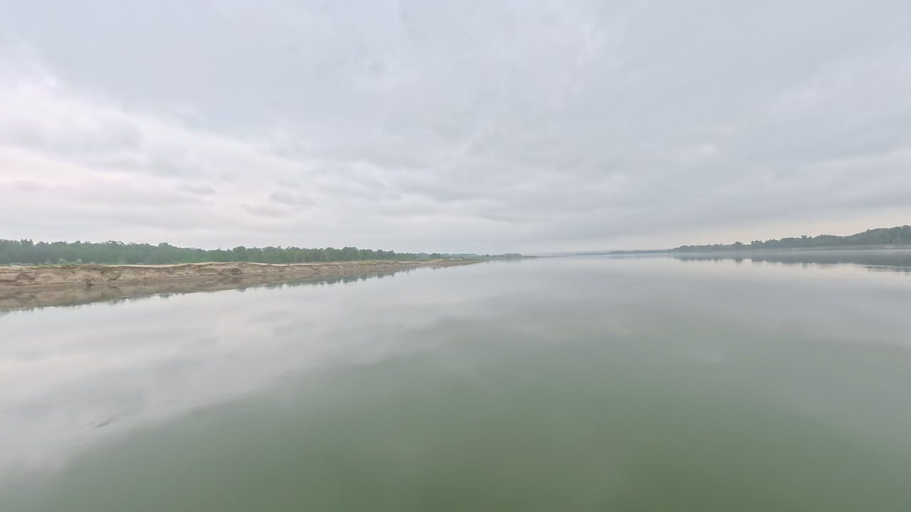 The calm Missouri River reflecting a grey sky, with a long sandbar on the left, 2025