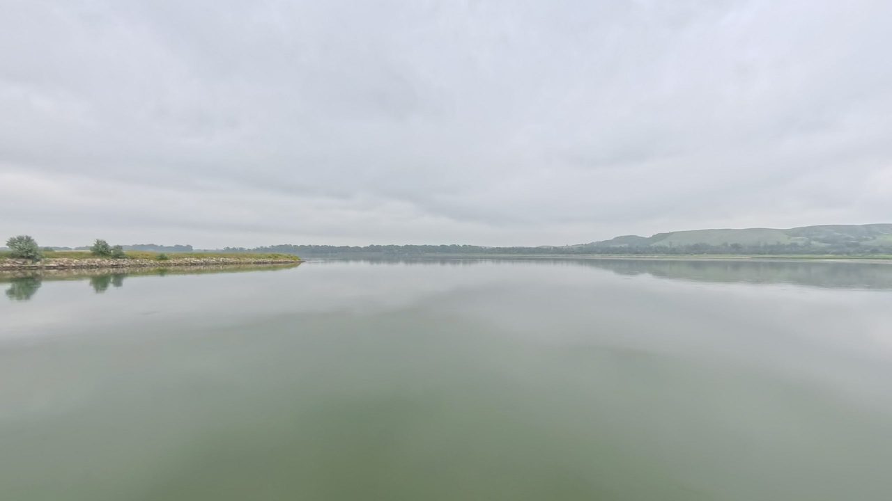 The calm Missouri River with a low wooded point on the left and hills in the distance, 2025