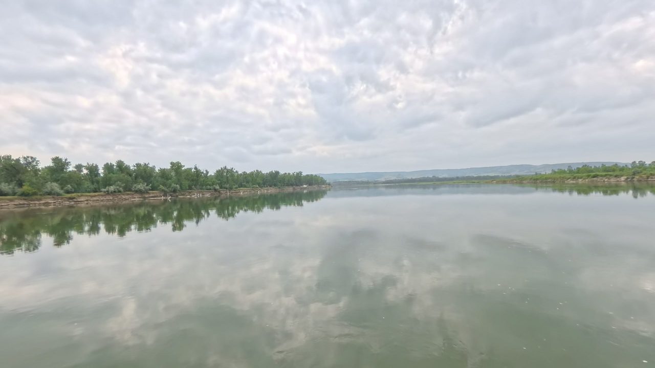 The calm Missouri River reflecting clouds, with a wooded point on the left, 2025
