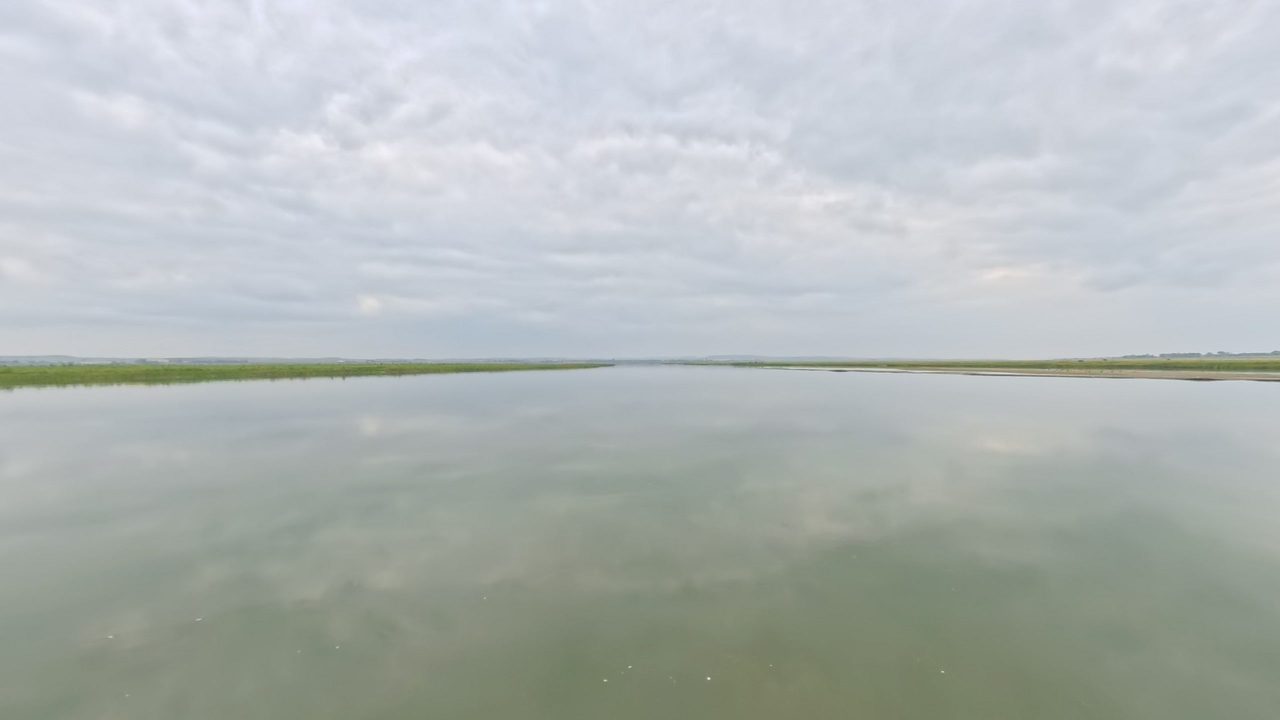 The calm Missouri River under a cloudy sky, with a long, low grassy shore, 2025