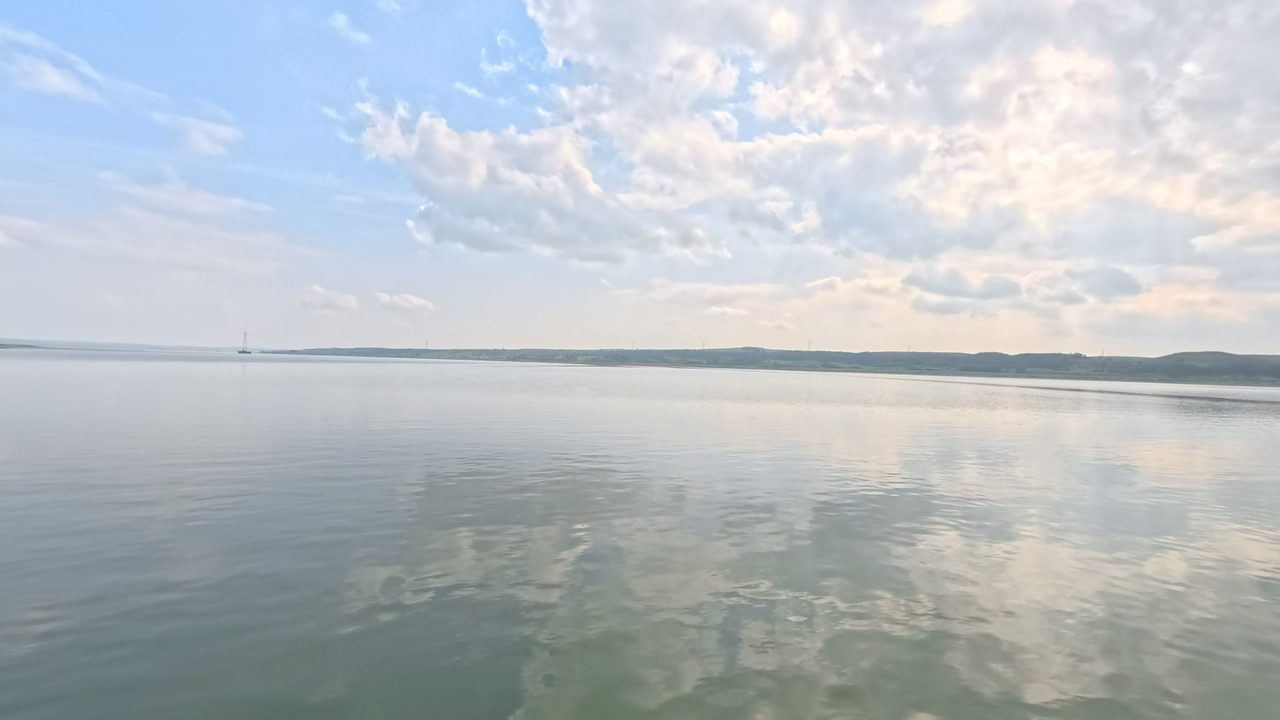 The calm Missouri River reflecting broken clouds, with low shores in the distance, 2025