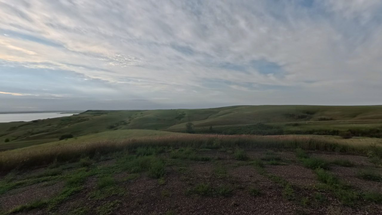Rolling grassy hills above the water of Lake Oahe, under a sky of streaked clouds, 2025