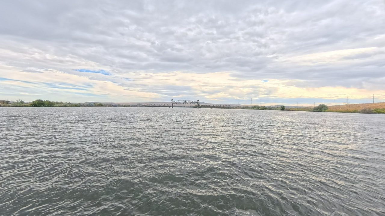 A wide, choppy river under a cloudy sky, with a steel lift bridge in the distance, 2025