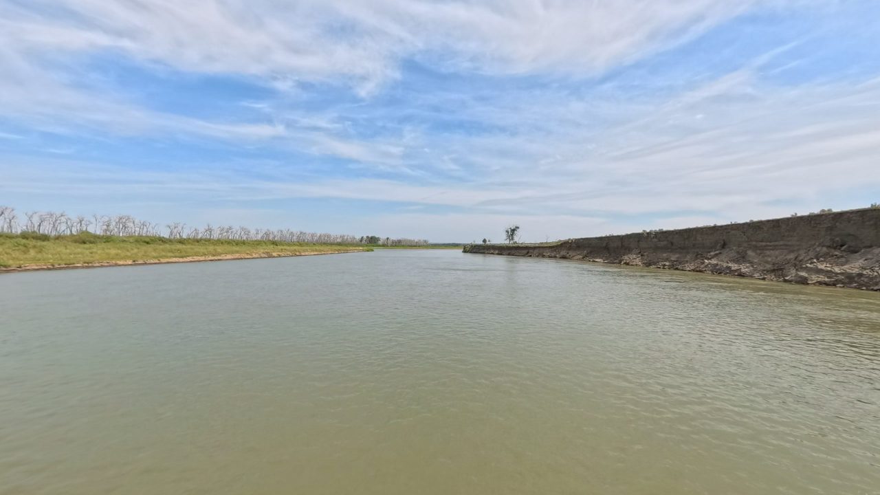 The Missouri River beside an eroded, dark bank on the right, with bare trees on the left, 2025