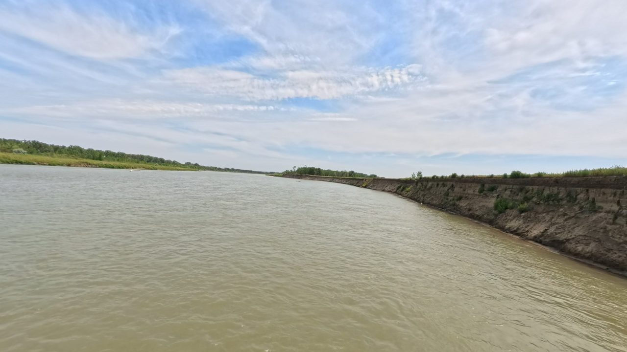 The Missouri River beside a steep, eroded right bank under streaks of cloud, 2025
