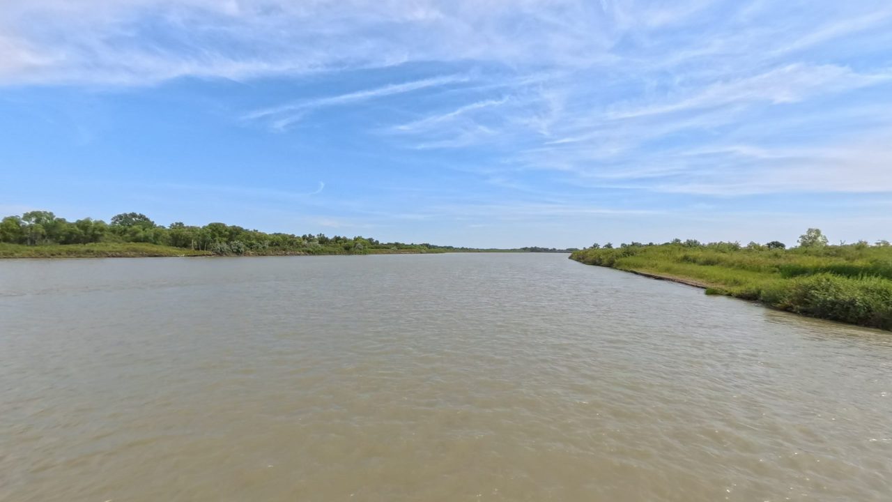 The wide Missouri River beside a low grassy bank on the right, under streaked clouds, 2025