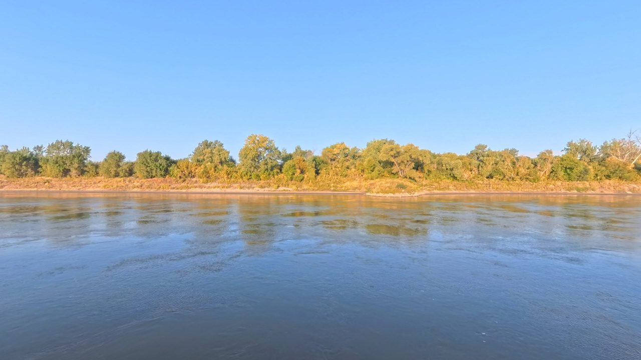 The Missouri River below a sandy bank and trees turning gold in warm, low sunlight, 2025