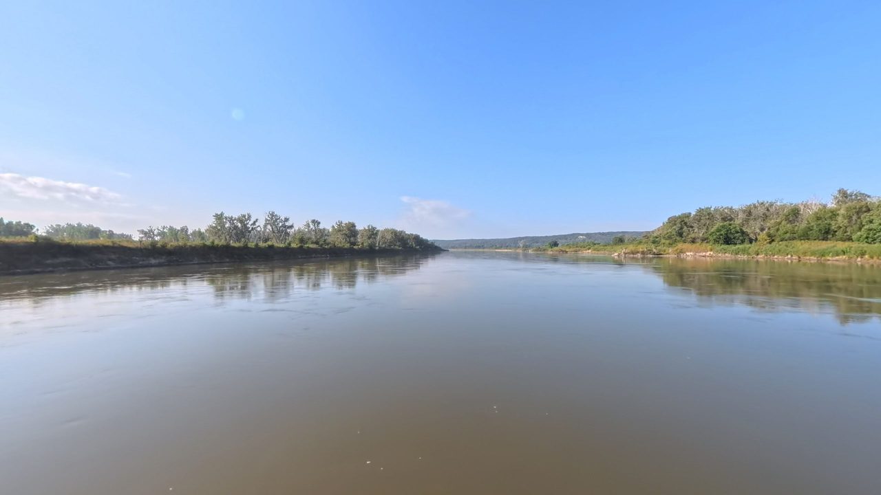The Missouri River between wooded banks under a clear blue sky, 2025