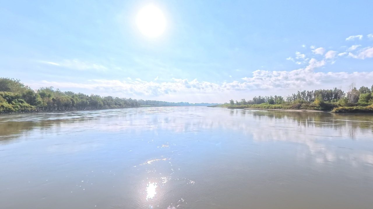 The Missouri River reflecting clouds between wooded banks under a bright sun, 2025