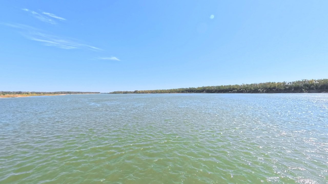The wide Missouri River in green water with a low wooded shore, under a clear sky, 2025