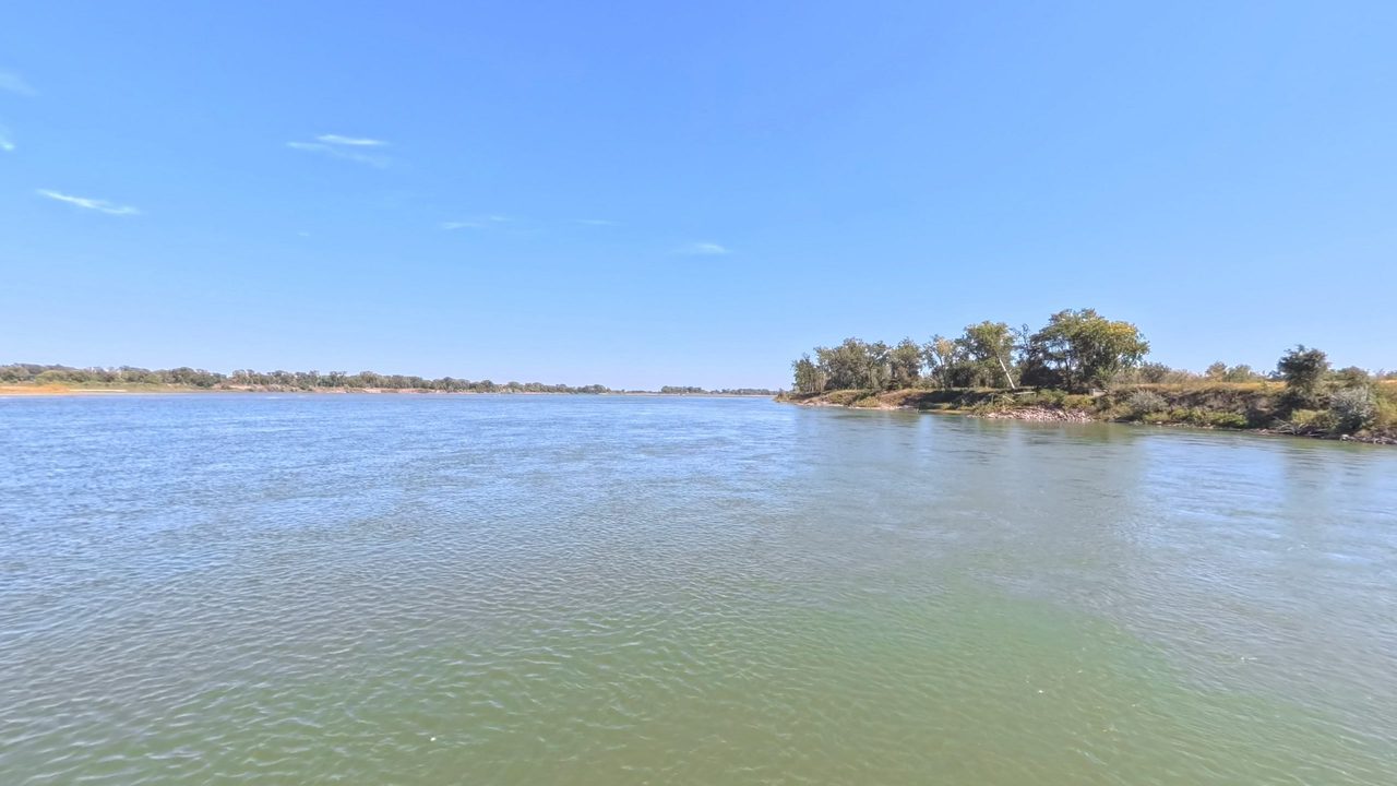 The Missouri River with a small wooded island on the right, under a clear sky, 2025