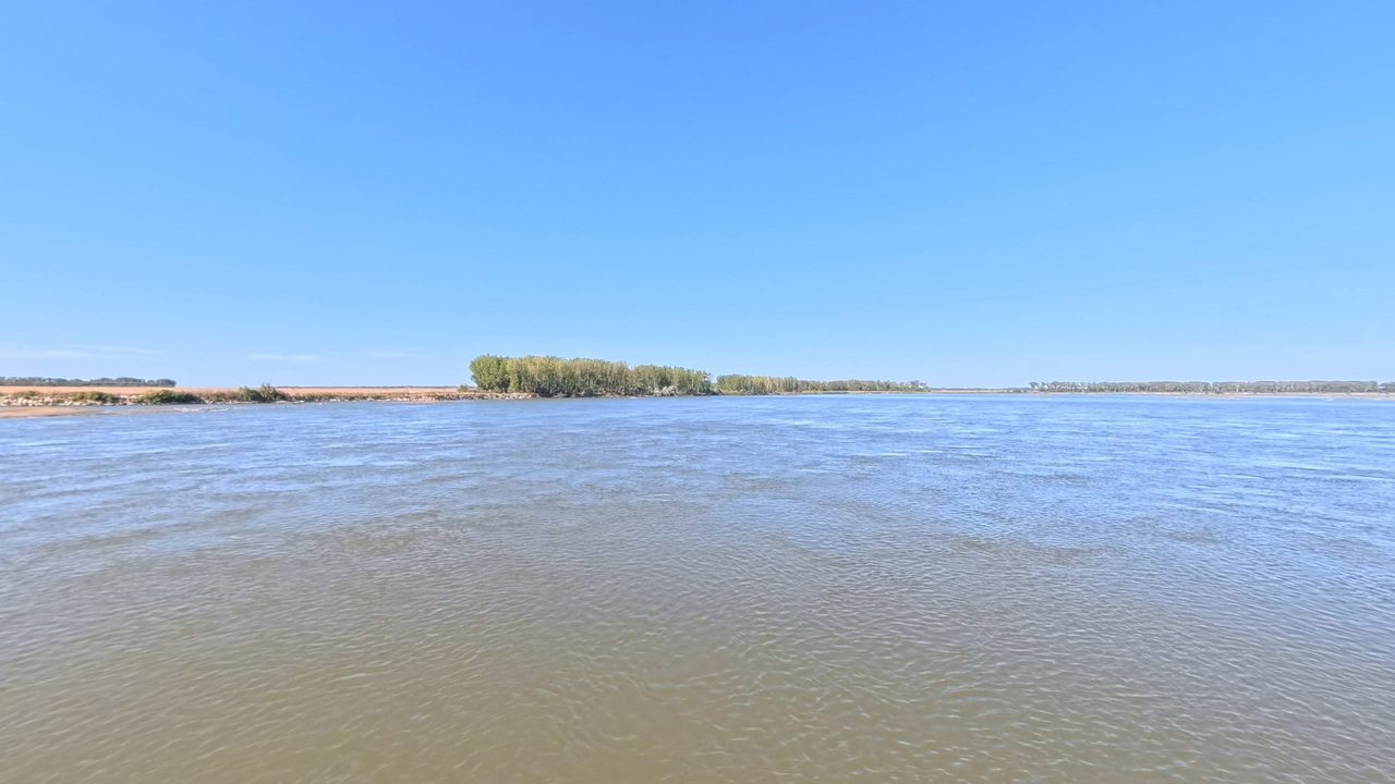 The wide Missouri River with a low wooded island in the distance, under a clear sky, 2025