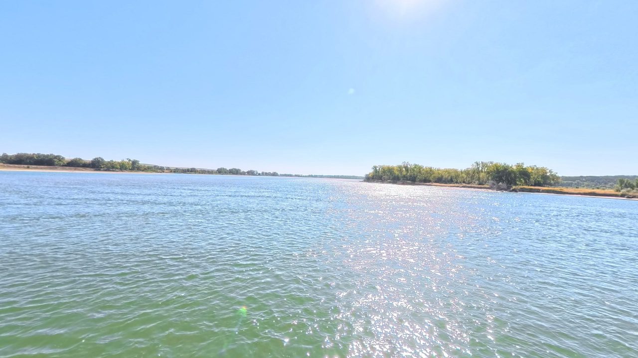 The wide Missouri River glittering under a bright sky, with a wooded island on the right, 2025