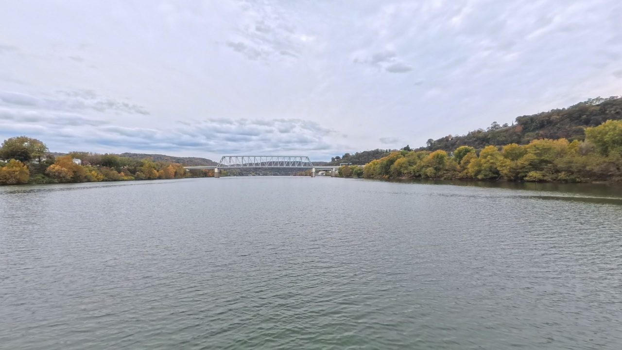 The Ohio River toward a distant truss bridge, with autumn woods on the right bank, 2025