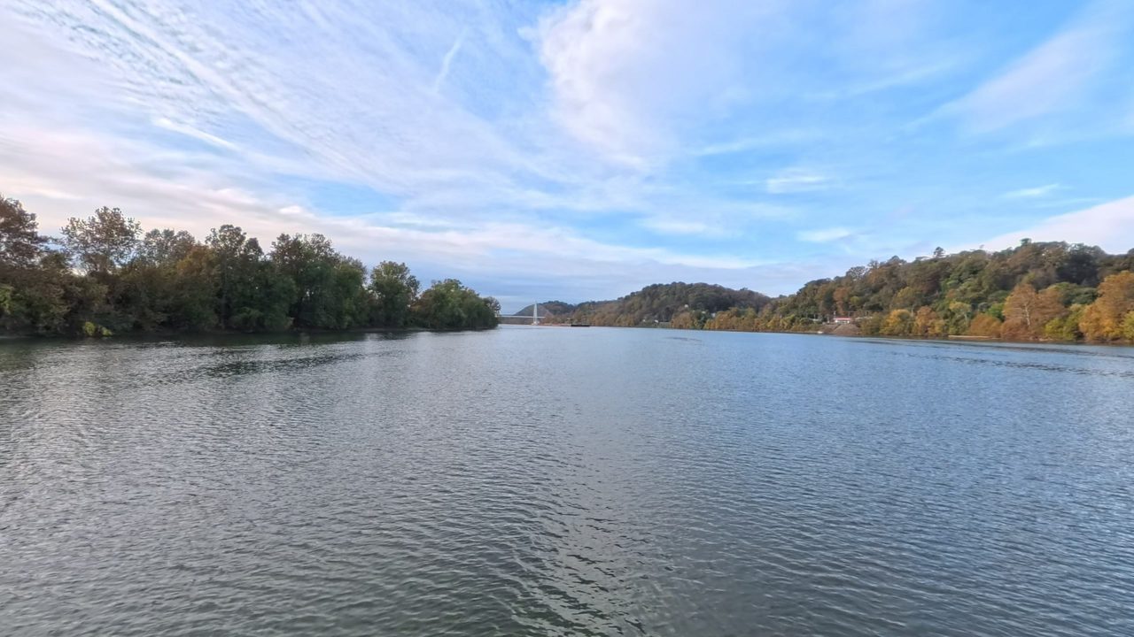 The Ohio River between an island of autumn trees and wooded hills, with a bridge tower in the distance, 2025