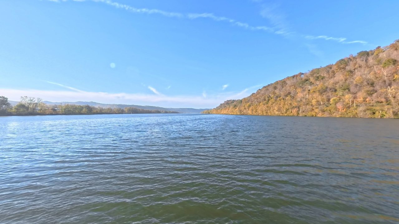 The broad Ohio River between hills in autumn color, under a blue sky with thin clouds, 2025