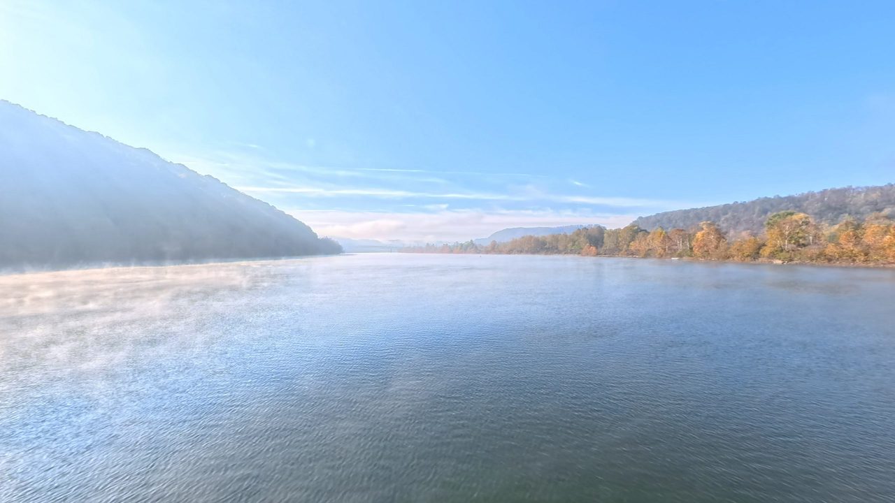 Morning mist on the Ohio River between wooded hills in autumn color, under a clear blue sky, 2025